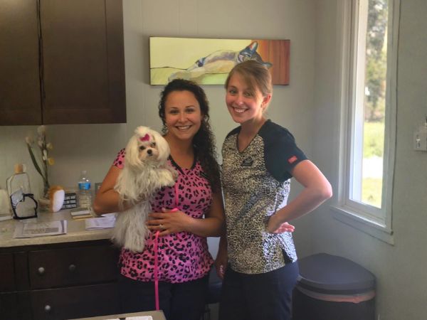 Two East Suburban Animal Hospital staff members posing with a small white dog in an exam room.